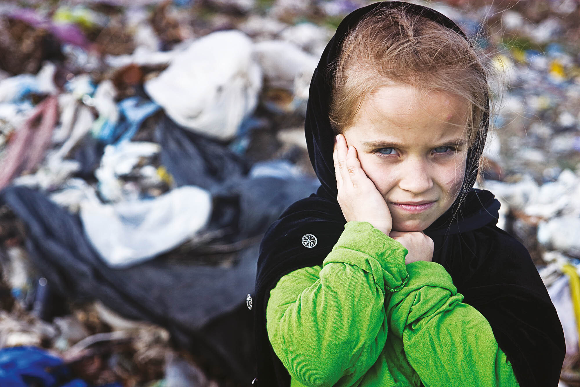 A beggar little girl in rags in a city dump close up