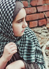 a refugee child in the war, a Muslim girl with a dirty face on the ruins, the concept of peace and war, the child is crying and waiting for help.